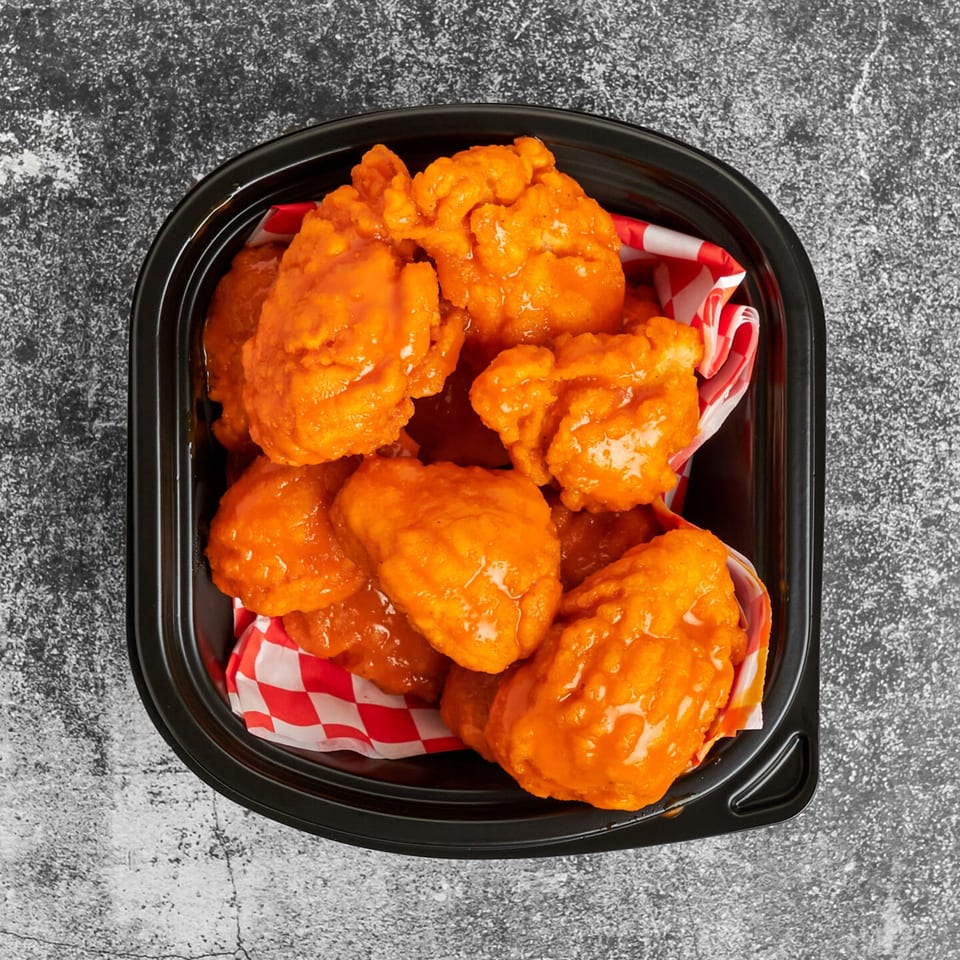 Trent's Pizzeria boneless wings, coated in bright orange buffalo sauce, served in a black container.