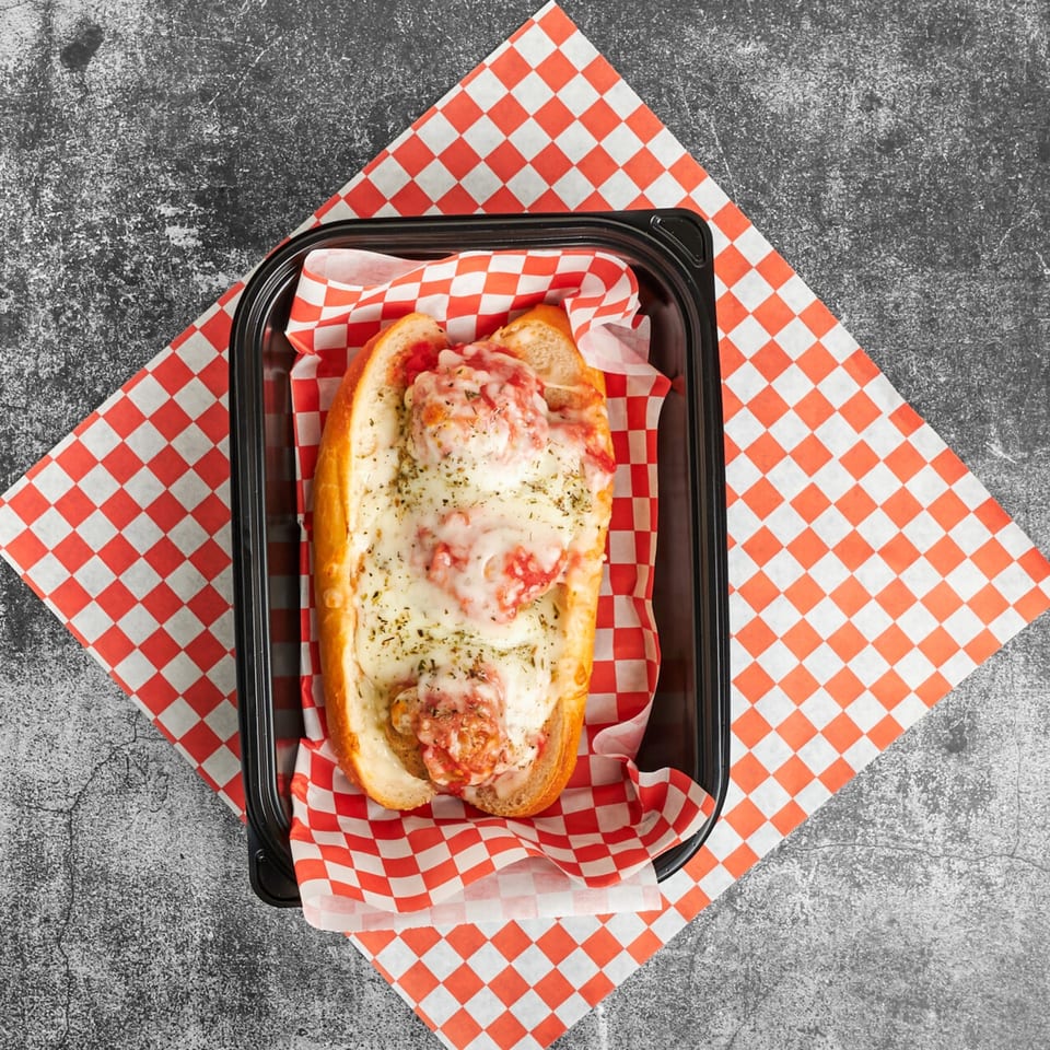 Trent's Pizzeria meatball sub with melted cheese and sauce in a black container on checkered paper.