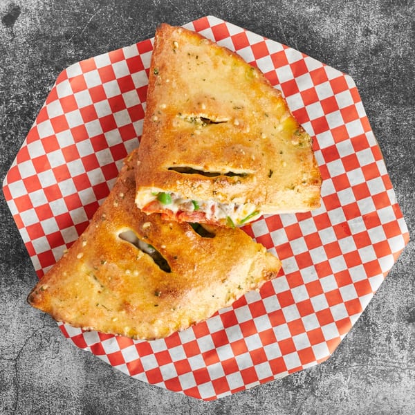 Two golden-brown calzones, filled with cheese and vegetables, on red and white checkered paper.